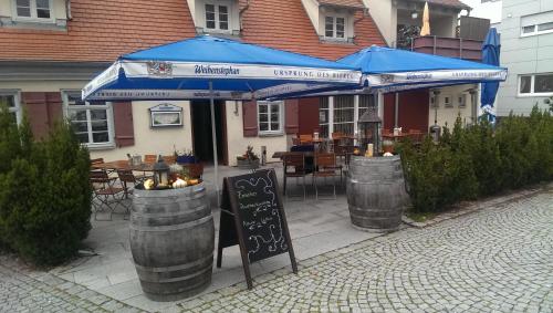 a restaurant with a blue umbrella and two barrels at Pension Webstuhl in Deizisau