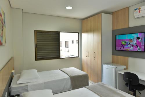 a bedroom with two beds and a desk and a tv at Hotel Plaza Garden in Cascavel