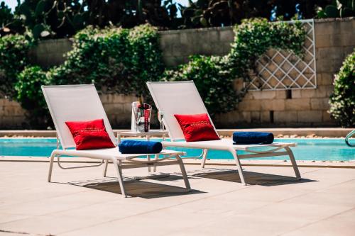 two white chairs with red and blue cushions next to a pool at The Xara Palace Relais & Chateaux in Mdina