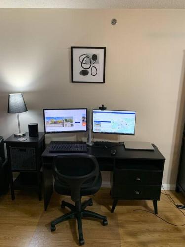a computer desk with two monitors and a chair at Chris Cozy Condo Commonwealth #205 Edmonton in Edmonton