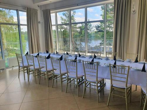 Lubiana Resort في Lubiana: طاولة طويلة مع طاولات بيضاء وكراسي في غرفة بها نوافذ