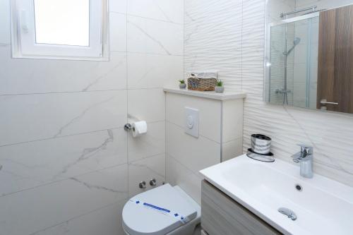 a white bathroom with a toilet and a sink at Apartments Vicin in Brela