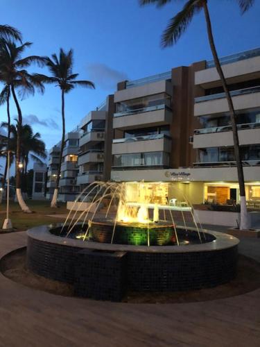 a fountain in front of a building with palm trees at Village pé na areia com limpeza in Lauro de Freitas