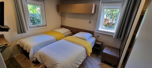 - 2 lits dans une petite chambre avec 2 fenêtres dans l'établissement Mobile home avec terrasse et piscine., à Hourtin