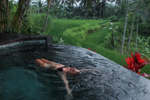 a person laying in a hot tub in the water at Masakali Retreat in Ubud