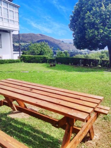 a wooden bench sitting in the grass near a house at Apartamentos Minas de Silvarosa in Viveiro