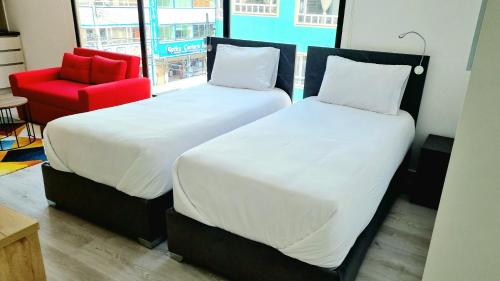 two beds in a room with a red chair at Toscana LOFT - Apartasuites in Bogotá