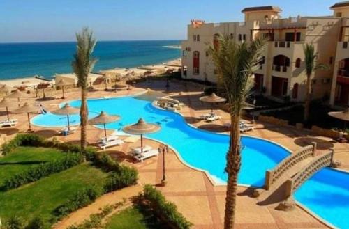 a resort with two pools and palm trees and the ocean at Lasirena North Coast in Mājid Abū Zayd