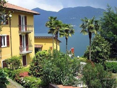 a yellow house with palm trees and mountains in the background at Albergo Del Lago in Cannobio