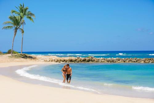 a man walking on the beach with a surfboard at Hyatt Zilara Rose Hall Adults Only - All Inclusive in Montego Bay