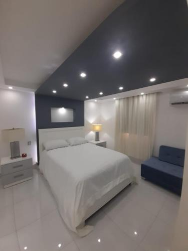 a bedroom with a large white bed and a blue couch at Hermoso apartamento Residencial madera I in Santiago de los Caballeros
