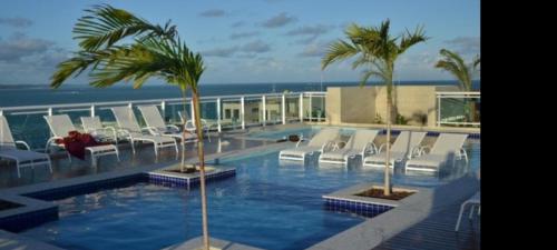 a swimming pool with chairs and palm trees on a building at Apartamento na praia de Jatiúca com piscina e área de lazer in Maceió