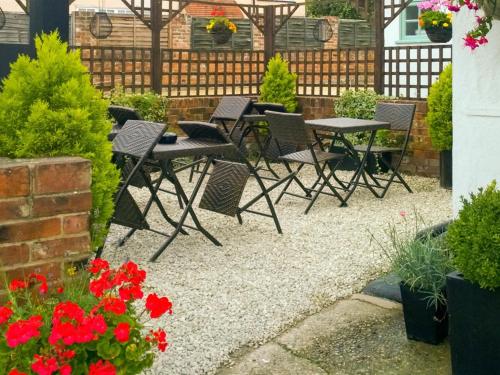 un patio con tavoli, sedie e fiori rossi di The Green Man Boutique Hotel a Takeley