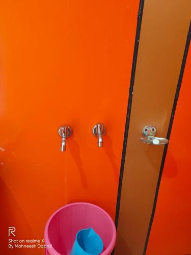 an orange wall with a pink bucket in a bathroom at Hotel Sunrise Inn & Restaurant, Kanatal in Chamba