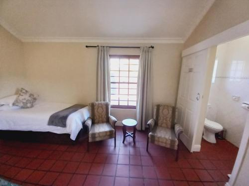 a bedroom with a bed and two chairs and a window at 137 High Street Guest House in Grahamstown