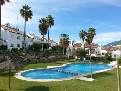 una piscina en un complejo con palmeras y casas en Casa Adosada Bel Andalus, en Estepona