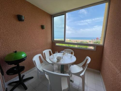 d'une salle à manger avec une table, des chaises blanches et une fenêtre. dans l'établissement Appartement avec piscine commune à 800 m Plage 5RH1155, à Saint Pierre La Mer
