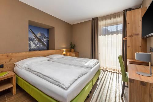um quarto com uma cama, uma secretária e uma janela em Hotel Vittoria - Ricarica l'anima em Dimaro