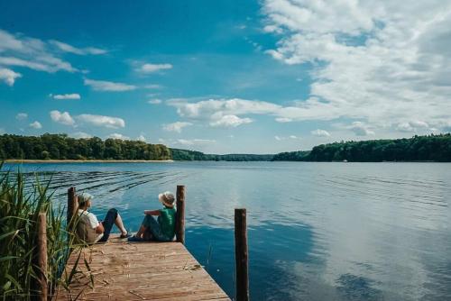 two children sitting on a dock on a lake at Holzhaus direkt am See in Priepert