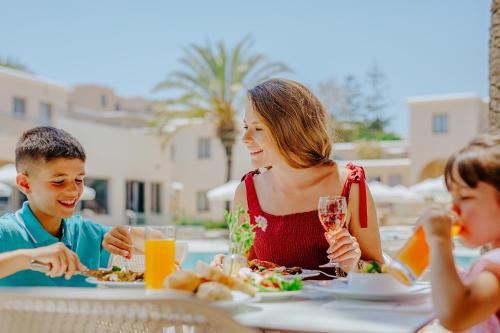 a woman and two children sitting at a table eating food at Louis St. Elias Resort & Waterpark in Protaras