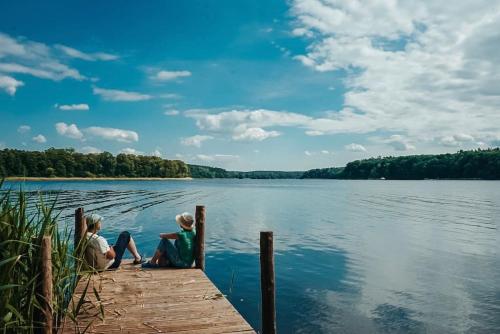 zwei Kinder sitzen auf einem Dock auf einem See in der Unterkunft Ferienzimmer direkt am See in Priepert