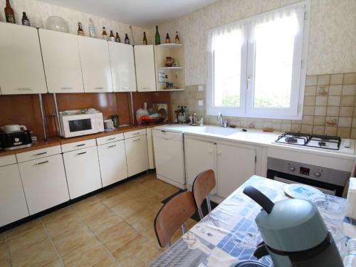 une cuisine avec des armoires blanches, une table et une fenêtre dans l'établissement Maison avec grand jardin clos, 6 couchages, proche forêt domaniale - Saint-Georges-d'Oléron - FR-1-246A-131, à Saint-Georges-dʼOléron