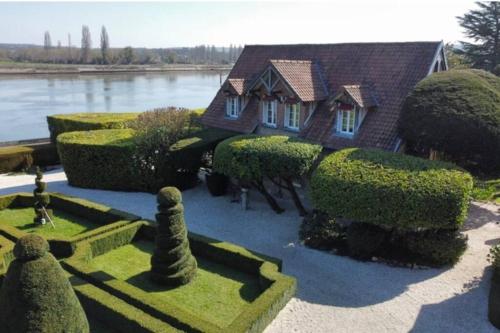 a house with a bunch of bushes in front of a lake at Le Clos des Roches in La Bouille