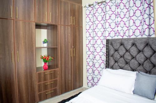 1 BR FULLY FURNISHED NAKA في ناكورو: غرفة نوم بسرير وخزانات خشبية و مزهرية بها ورد