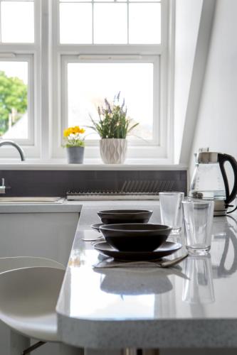 a kitchen counter with plates and glasses and two windows at Beach View Luxury Apartment in Lyme Regis