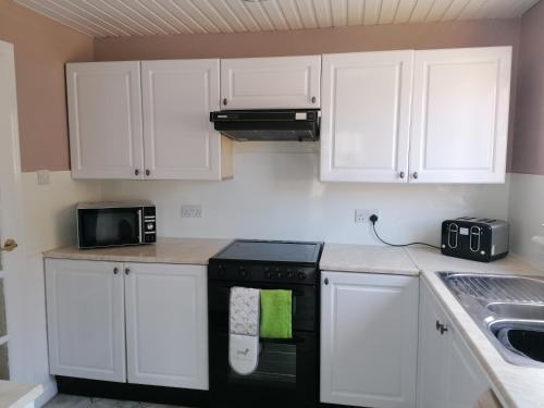 una cocina con armarios blancos y un aparato negro en Beautiful three bedroom seaside retreat, en Prestonpans