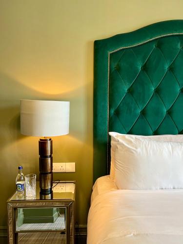 a bed with a green headboard and a table with a lamp at Magmell Townhouse in Baltinglass