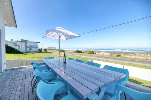 a wooden table with blue chairs and an umbrella at Klein Steenbok in Agulhas