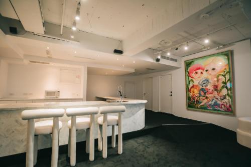 a kitchen with a bar with white stools and a painting at 苓旅松山館 Lininn Tapei Arena in Taipei