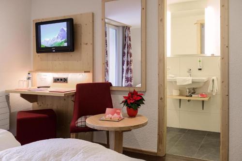 a room with a bed and a desk with a television at Hotel Caprice - Grindelwald in Grindelwald