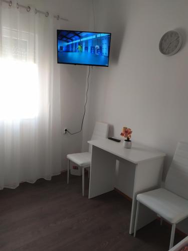 Habitación con mesa blanca, sillas y TV en la pared. en Apartman LEO, en Bečej