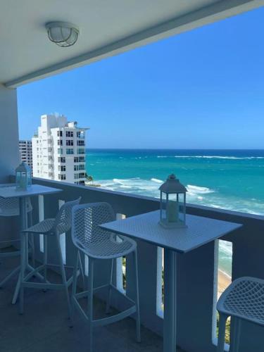 a balcony with tables and chairs and the ocean at KASA Blue Ocean - 2 bed 2 bath for 4 OCEAN VIEW BALCONY BEACHFRONT CONDO POOL in San Juan