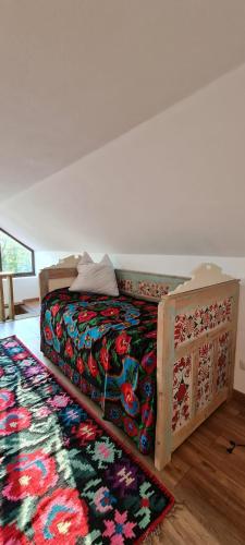 a bedroom with a bed with a colorful blanket and a rug at Acul în carul cu fan in Pădurenii