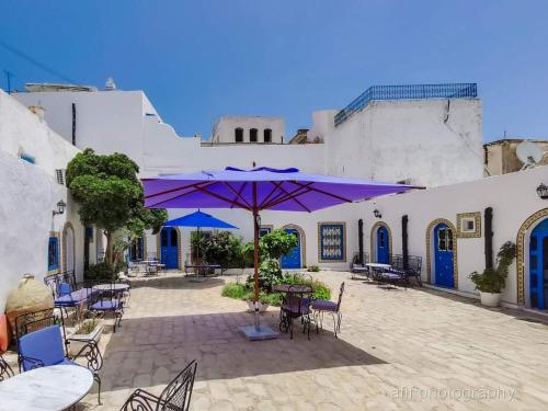 a patio with tables and chairs and a purple umbrella at Hôtel Bou Fares in Sidi Bou Saïd
