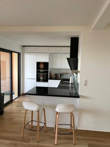 une cuisine avec un comptoir noir et deux tabourets dans l'établissement Superbe appartement neuf de haut standing, à Ajaccio