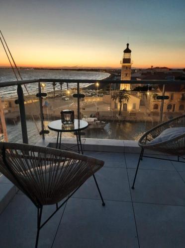 d'un balcon avec une table, des chaises et un phare. dans l'établissement Le Phare du Grau Superbe Appartement Standing 3 chambres vue Mer, au Grau-du-Roi