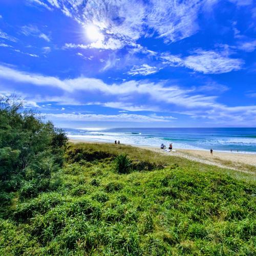 a beach with people on the sand and the ocean at Serene Beachside Apartment in Marcoola