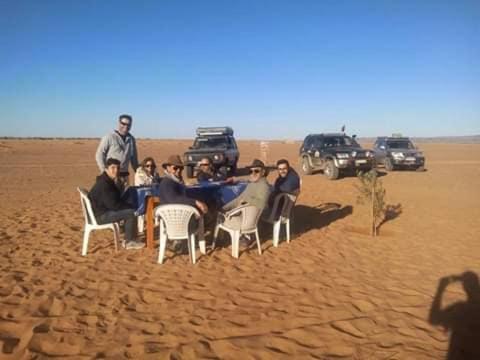 a group of people sitting around a table in the desert at Auberge Dinosaur Kem Kem in Tafraoute Sidi Ali