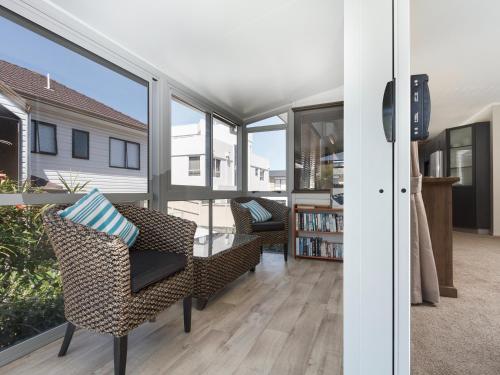 a living room with chairs and a table and windows at At The Bay - Mt Maunganui Holiday Home in Matapihi