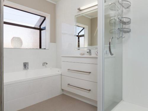 un bagno bianco con vasca, lavandino e specchio di At The Bay - Mt Maunganui Holiday Home a Matapihi