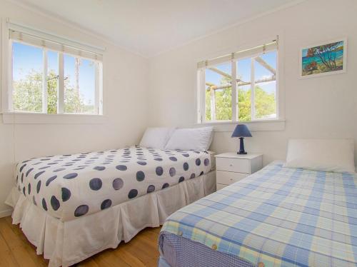 two beds in a bedroom with two windows at Daisy Cottage - Hahei Bach in Hahei