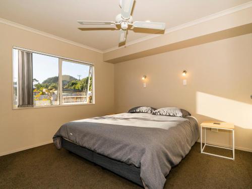a bedroom with a bed with a ceiling fan and a window at Home Base - Cooks Beach Holiday Home in Cooks Beach
