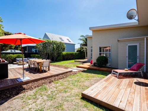 a backyard with a wooden deck with a table and an umbrella at Magnifique - Mangawhai Holiday Home in Mangawhai