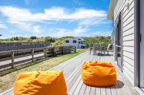 two orange chairs on a deck with a rv in the background at Beach Retreat - Ohope Holiday Home in Ohope Beach