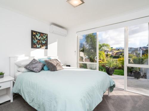 a white bedroom with a bed and a large window at Little Pearl of Vista Verano - Mangawhai Home in Mangawhai