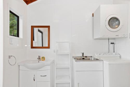 a white bathroom with two sinks and a mirror at Riverview Retreat - Cooks Beach Holiday Home in Cooks Beach